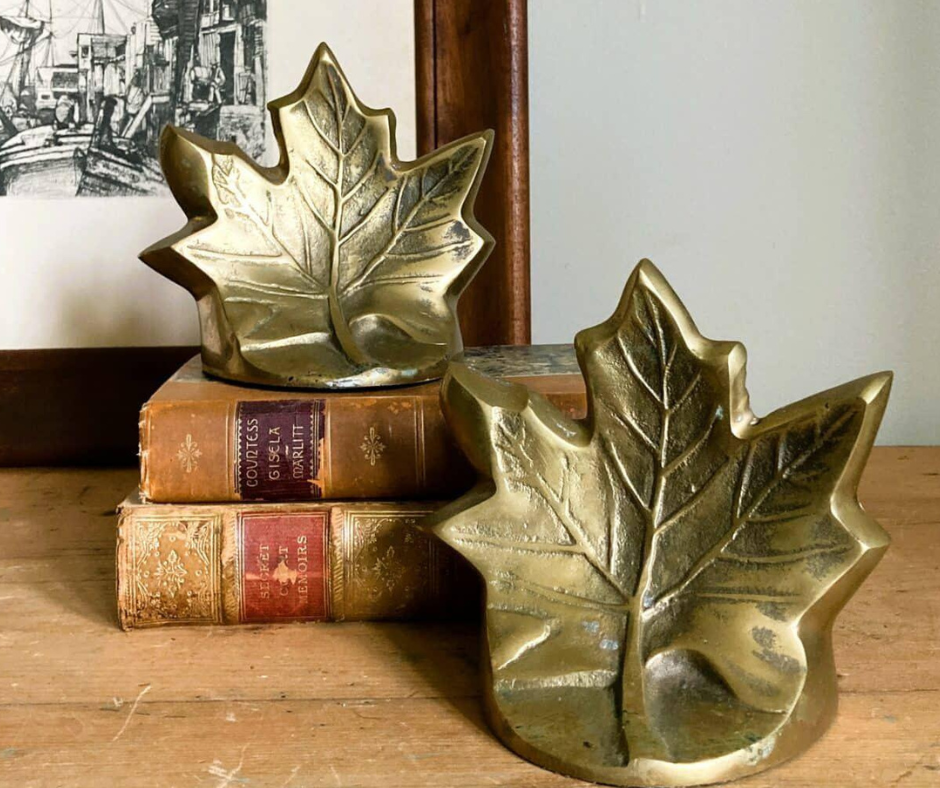 bronze leaf statues propped on autumnal colored books on a wooden shelf